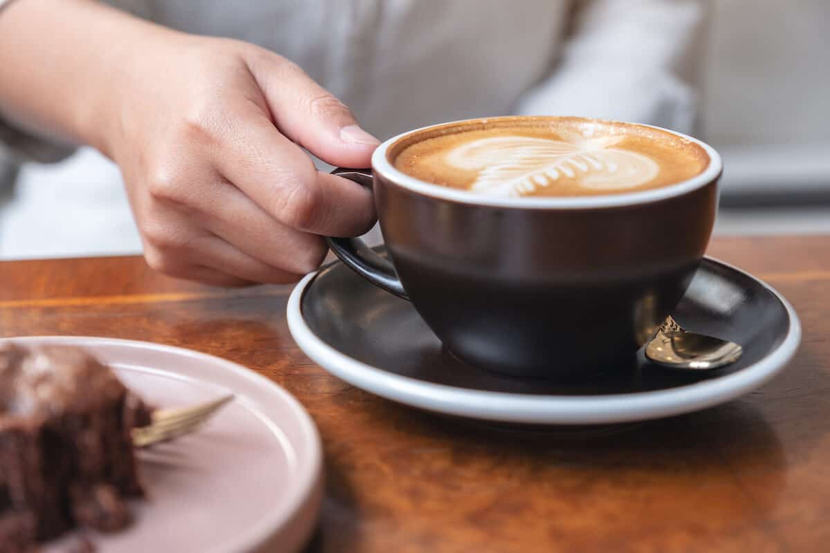 hand holding hot oat milk latte with latte art