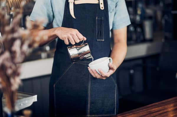 barista pouring oat milk into mug