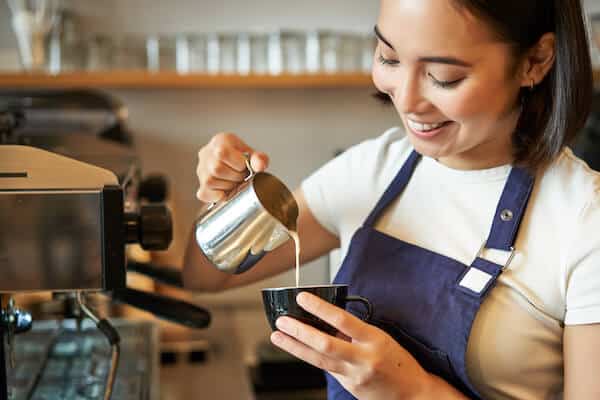 smiling barista making coffee drink with oat milk