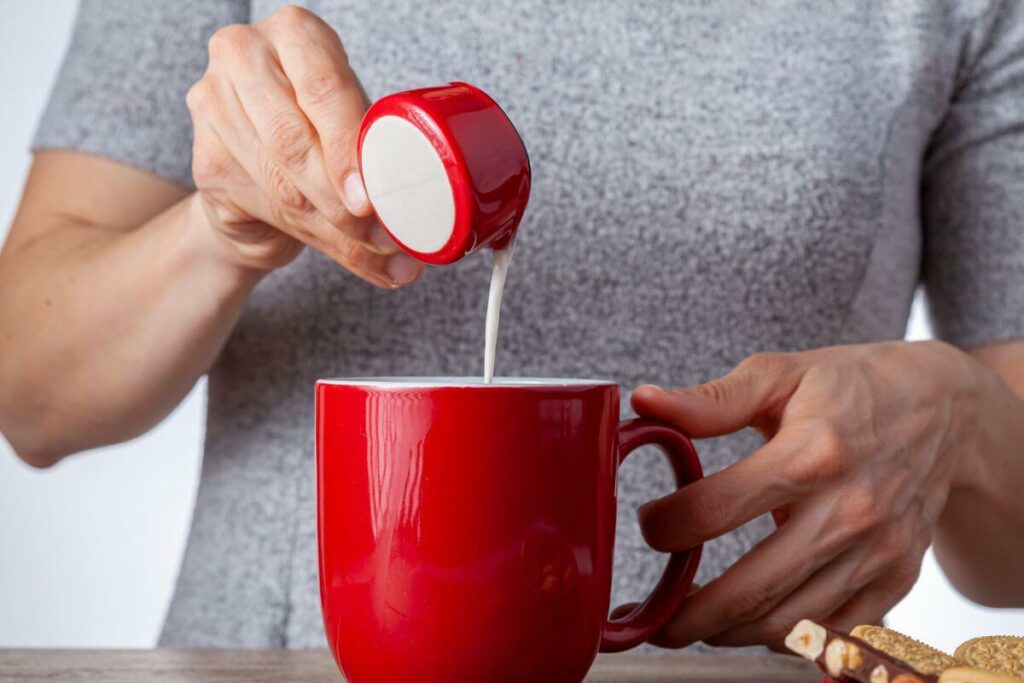 coffee creamer being poured into a red mug